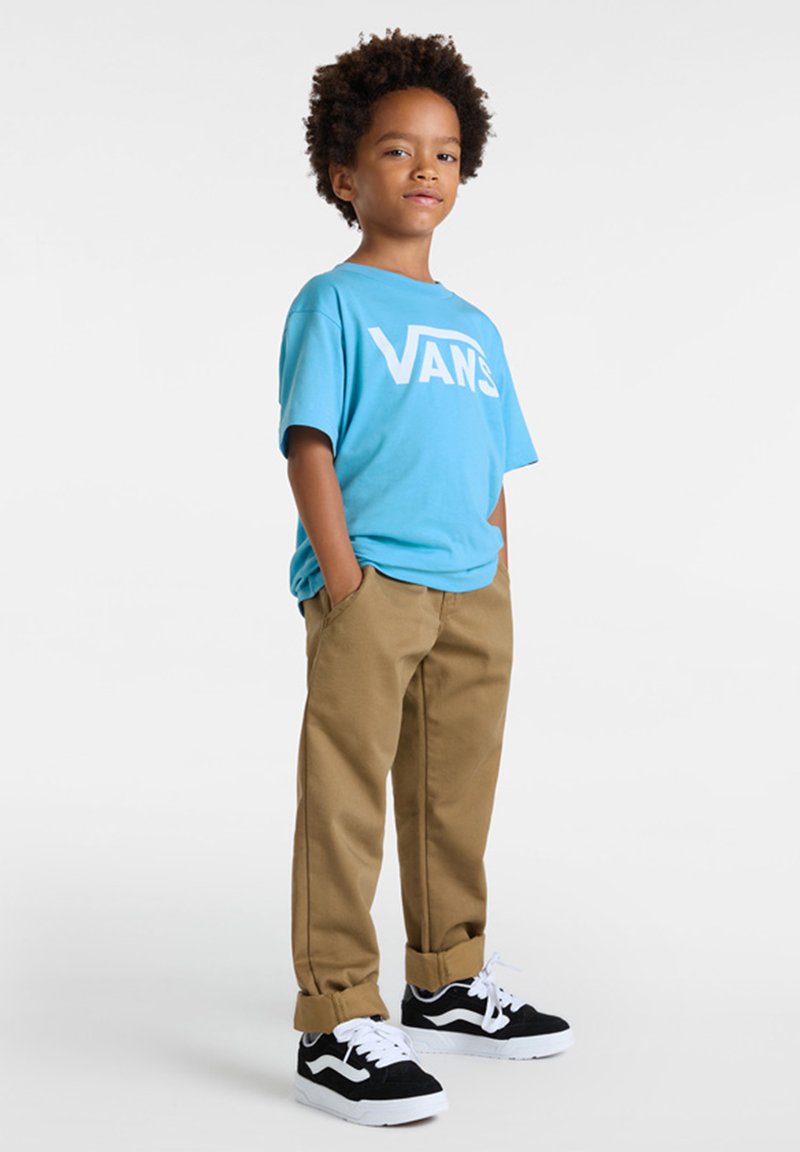 Modrý bavlněný tričko s velkým bílým logem "VANS", khaki kalhoty a černo-bílé tenisky se šněrovacím designem a klasickým vzorem.