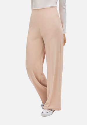 Pantalones de pierna ancha beige combinados con zapatillas blancas y una camiseta blanca de manga larga, mostrando un estilo casual y relajado.