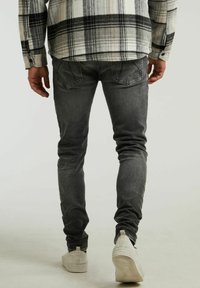 Jeans grises ajustados con una textura desgastada, diseño de cinco bolsillos y un sutil detalle de arrugas, combinados con calzado blanco.