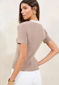 Top tricotat cu nervuri, de culoare bej deschis, cu un design mulat, mâneci scurte și un contrast subtil la decolteu. Textură netedă, detalii minime.