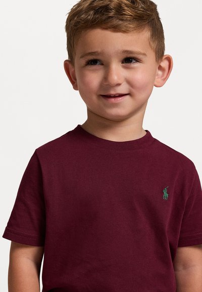 Μπλούζα βαμβακερή χρώματος μπορντό με κοντά μανίκια, με έναν μικρό πράσινο λογότυπο στην αριστερή πλευρά του στήθους. Λείος υφασμάτινος τύπος και κλασικό σχέδιο γύρου λαιμού.