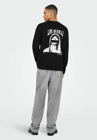 Maglietta nera a maniche lunghe con una grande grafica bianca sul retro con il testo "Lose Yourself", abbinata a pantaloni larghi grigi chiari.