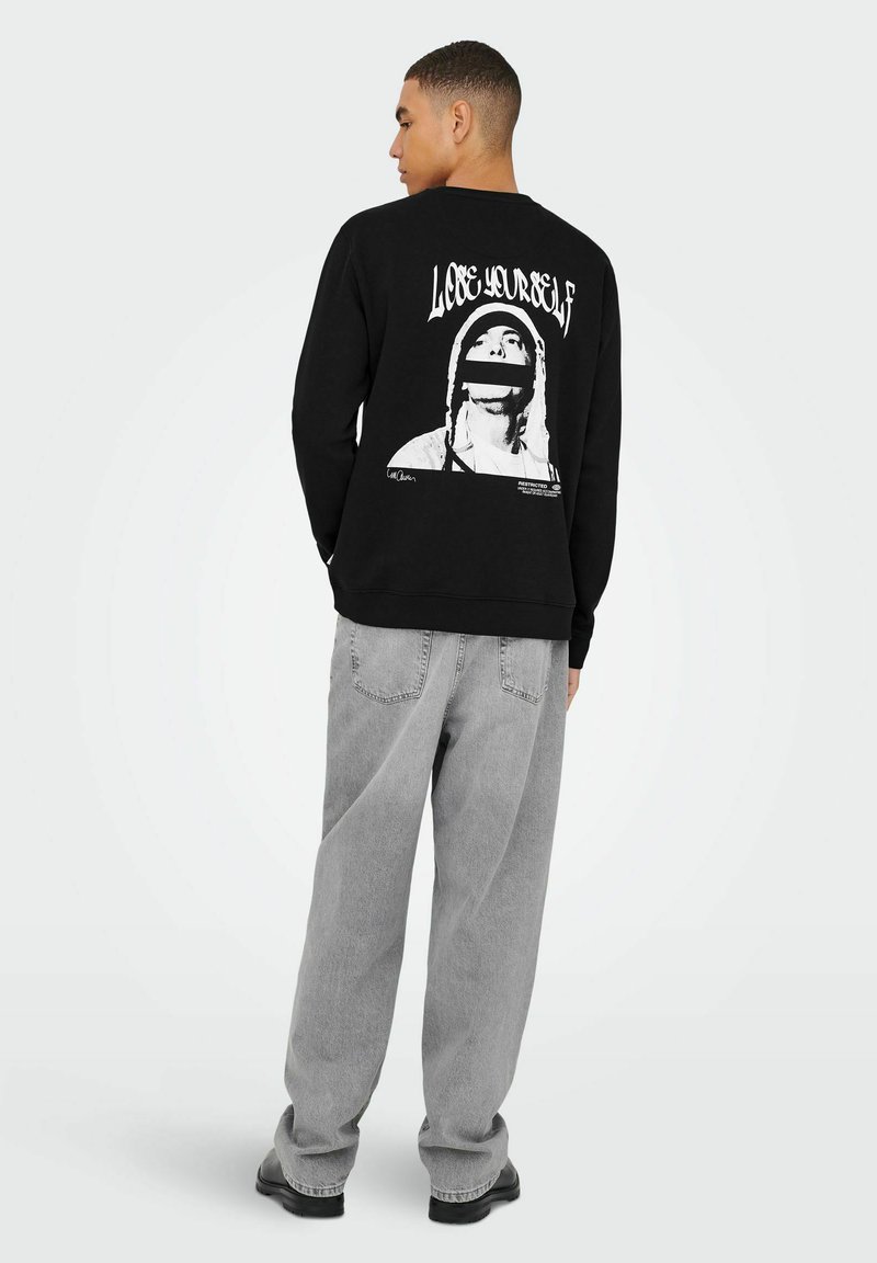 Maglietta nera a maniche lunghe con una grande grafica bianca sul retro con il testo "Lose Yourself", abbinata a pantaloni larghi grigi chiari.