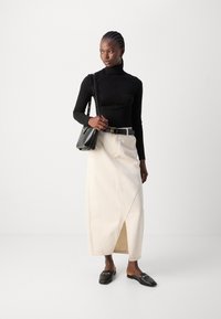 Zwarte geribde coltrui, lichtbeige lange rok met zijsplit en zwarte loafers. Gecombineerd met een kleine zwarte handtas en een riem.
