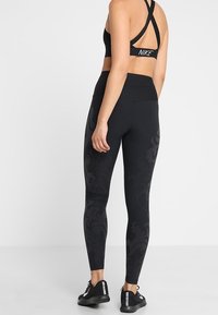 Svart sportbh med korsryggdesign, kombinerad med svarta leggings som har ett strukturerat blommönster. Båda gjorda av elastiskt material.