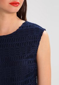 Navy blue sleeveless top with textured crochet design, featuring circular patterns and open weave details on fabric.