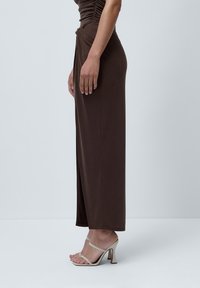 Brun kjole med tilpasset fasong, rynket bryst, sidefolding og lang lengde, parret med beige stroppehæler med kraftig hæl.
