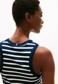 Camiseta de tirantes de canalé a rayas en azul marino y blanco, con escote redondo y un pequeño detalle de tres colores en la parte posterior. Textura suave.