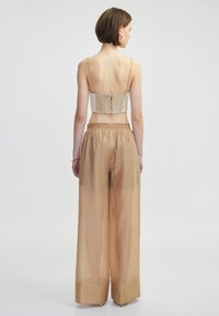 Beige doorschijnende wijde broek met een elastische tailleband, gecombineerd met een rugloze top met een ingewikkeld bedrukte ontwerpen in een lichte kleur.