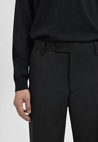 Pantalons noirs sur mesure en tissu lisse, avec fermeture à bouton, passants de ceinture et coupe droite.