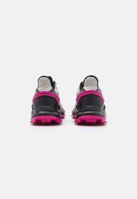 Scarpe sportive nere e grigie con una suola rosa e dettagli rosa sul tallone, caratterizzate da una superficie testurizzata e un design del tallone rinforzato.