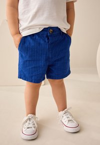 Pantalones cortos de rayas azules hechos de tela con acabado texturizado, con cierre de botón y bolsillos, combinados con zapatillas blancas.