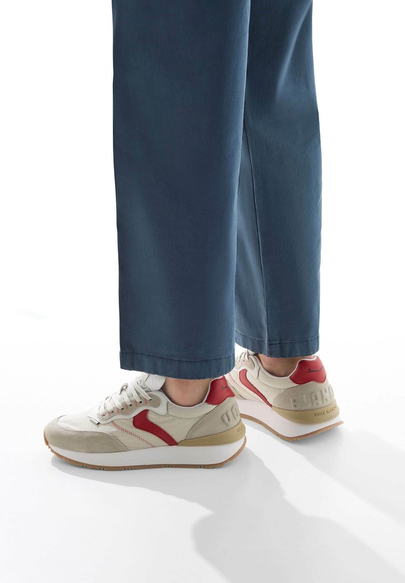 Sneakers beige con accenti rossi, materiali in suede e mesh, design con lacci, suola bianca con battistrada in gomma e logo sul tallone.
