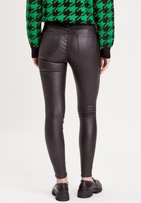 Pantalons skinny en simili cuir noir avec poches arrière et coutures, associés à des chaussures noires à semelle épaisse ; texture lisse.