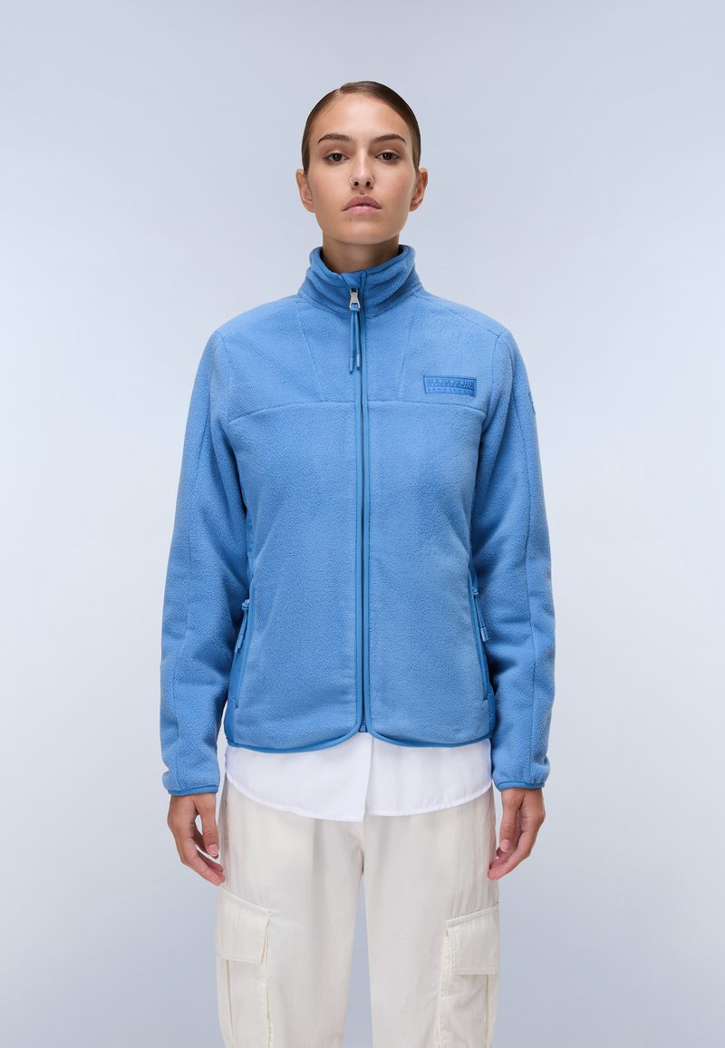 Giacca in pile azzurro chiaro con colletto alto, chiusura con zip e due tasche laterali. Tessuto liscio con dettagli delle cuciture a contrasto.