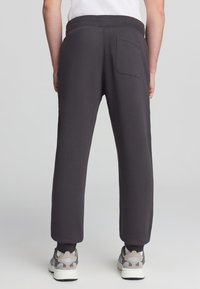 Ciemnoszare dresy z elastycznym paskiem, zwężanymi nogawkami i jedną tylną kieszenią, uszyte z miękkiego materiału. Niezakończony brzeg przy kostkach.