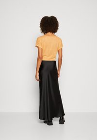 Oranje metallic kortekleedshirt gecombineerd met een zwarte satijnen maxi-jurk. De outfit heeft een soepele, vloeiende textuur en een minimalistisch ontwerp.