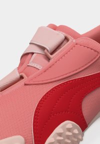 Κοντινό πλάνο ροζ και κόκκινου αθλητικού παπουτσιού με διχτυωτό ύφασμα, λουρί με βέλκρο και λεπτομέρειες στην υφή της σόλας σε λευκό φόντο.