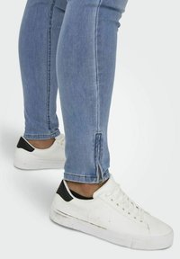 Biele tenisky s čiernymi detailmi, textúrovaná podošva, spárované so svetlomodrými slim fit džínsami s detailmi na zipsoch pri členkoch.
