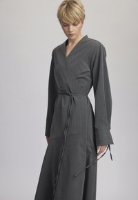 Rochie gri cu dungi verticale, mâneci lungi și talie legată. Prezintă un decolteu în V adânc și o fustă evazată cu un design stratificat.