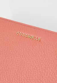 Roze gestructureerde leren portemonnee met het in goud geperste "COCCINELLE" logo. Soepele stiksels zichtbaar langs de randen.