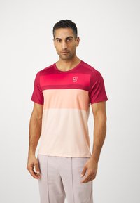 Rød og ferskenfarget gradient treningsskjorte med rund hals og korte ermer, med en liten logo på brystet og jevn tekstur.