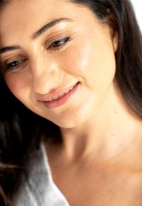 Close-up van een persoon met donker haar, een egale huid en een lichte teint, gekleed in een wit kledingstuk. Focus op de gelaatstrekken en expressie.