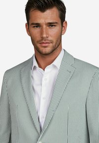 Gestreepte blazer in lichtgroen en wit, met een notch-lapel, sluiting met één knoop en een gestructureerde stof. Gecombineerd met een wit overhemd hieronder.