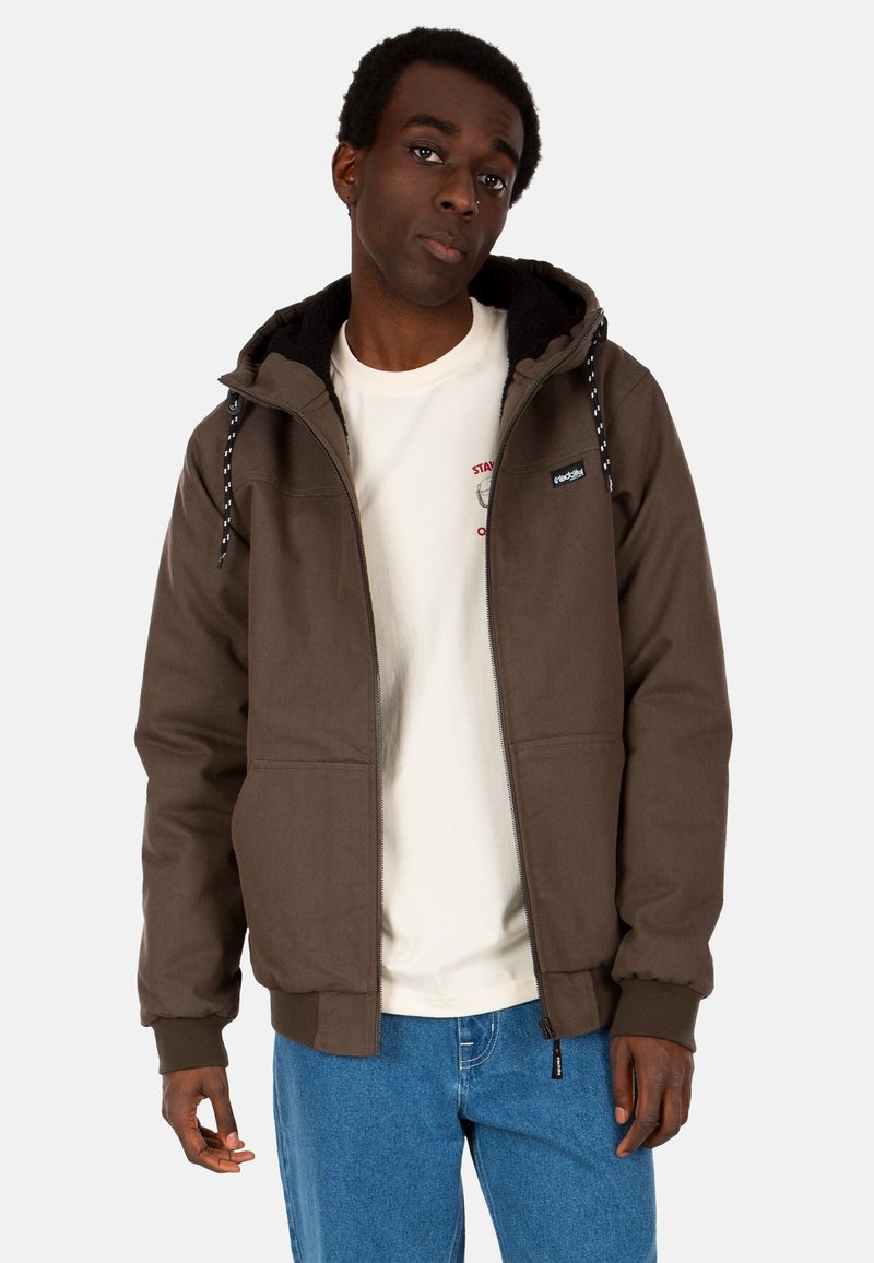 Braune Zip-Jacke mit Kapuze, ausgestattet mit einem Fleece-Innenfutter und Kordelzügen. Getragen über einem cremefarbenen T-Shirt und blauen Jeans.