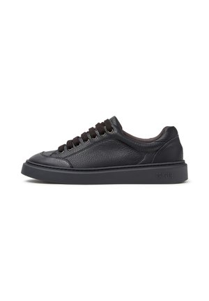 Schwarzer flacher Ledersneaker mit schwarzen Schnürsenkeln und dicker Sohle, Seitenansicht zeigt strukturiertes Material und Markennamen auf der Sohle.