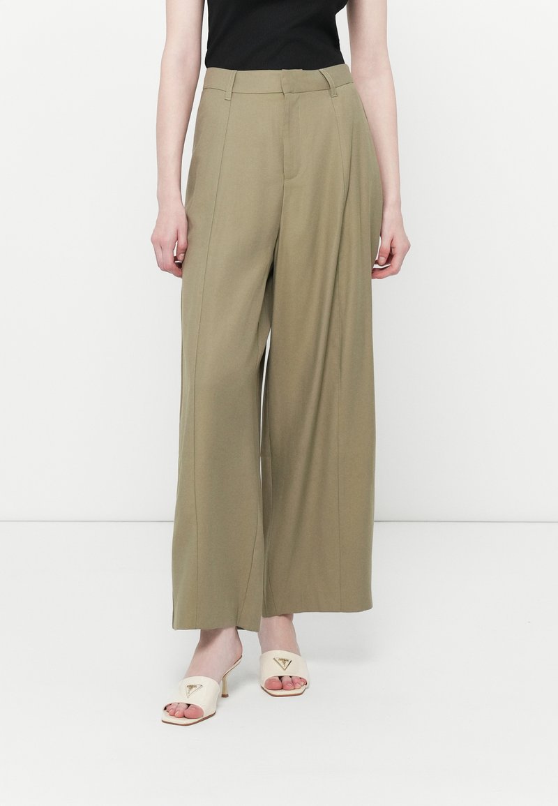 Olivengrønne bukser med brede ben og høj talje, struktureret design og frontfold. Kombineret med beige åben tå hæle med logo detajle.