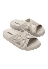 Des sandales beiges à enfiler présentant un design en point de croix avec un marquage "Melissa" en relief, fabriquées en caoutchouc doux avec une semelle texturée.