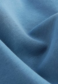 Cotton fabric in a soft, muted blue color; smooth texture with fine knit pattern and subtle sheen. Folded to show depth and form.