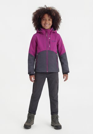 Enfant souriant aux cheveux bouclés portant une veste à capuche violette et grise, un pantalon cargo gris et des bottes de randonnée grises, debout avec les bras détendus.