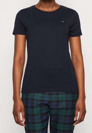 Granatowy dopasowany t-shirt z krótkim rękawem z małym logo na piersi, noszony z zielono-niebieskimi spodniami w kratę.