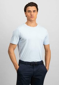 Tricou scurt, de culoare albastru deschis, confecționat din bumbac, cu un guler rotund. Poartă pantaloni bleumarin și o curea țesută. Design simplu, fără modele.