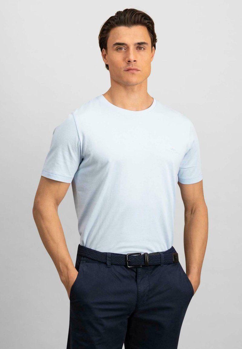 Tricou scurt, de culoare albastru deschis, confecționat din bumbac, cu un guler rotund. Poartă pantaloni bleumarin și o curea țesută. Design simplu, fără modele.