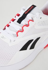 Sapatilha atlética branca com detalhes em preto e vermelho, parte superior em malha, design em zigue-zague na lateral e logótipo em destaque na lingueta.