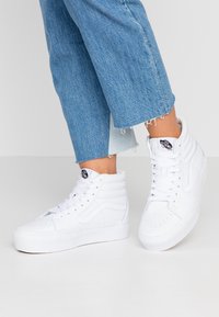 Vita högklackade sneakers av slätt läder med vadderade kragar, runda tår och signaturlogotaggar på tungan. Bärs med korta blå jeans.
