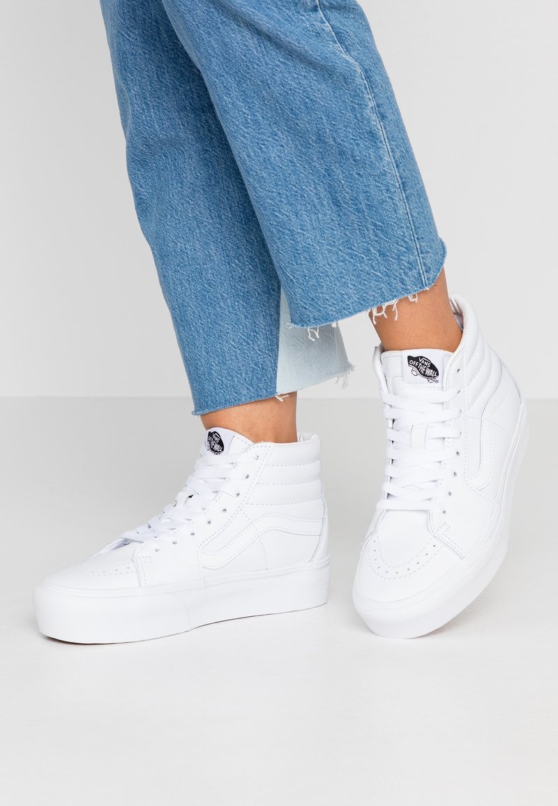 Witte hoge sneakers van glad leer met gewatteerde kraag, ronde neuzen en kenmerkende logotags op de tong. Gecombineerd met cropped blauwe denim.