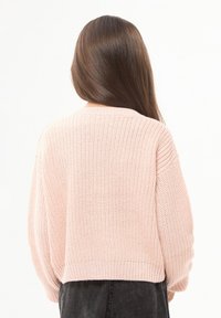 Jasnoróżowy sweter z dzianiny, krótki krój, szerokie rękawy, ribbowa dolna krawędź, fakturowany wzór, noszony na ciemnym podkładzie, widok z tyłu.