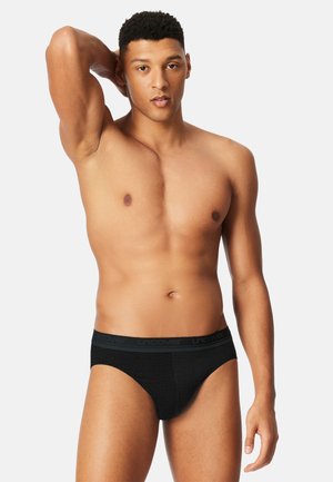 Black mesh men's briefs with a logoed waistband, featuring a snug fit and smooth texture, worn by a model with a neutral expression.