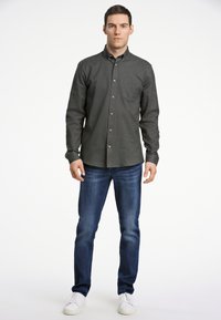 Grijze overhemden met een borstzak, gecombineerd met donkerblauwe spijkerbroeken en witte sneakers. Het shirt heeft een gestructureerde stof en bruine knopen.
