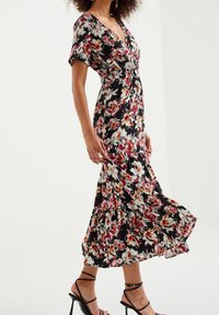 Blommig maxiklänning med svart botten, med röda och vita blommönster, V-ringning, korta ärmar och vågig volangnederkant.