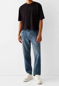 Svart kortärmad T-shirt kombinerad med ljusblå raka jeans och vita sneakers. Avslappnad outfit med en lätt passform och minimal design.