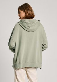 Hoodie overtaglia in cotone verde chiaro, con cappuccio regolabile, spalle scese e spacchi laterali all'orlo per un maggiore comfort.