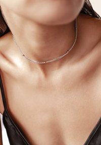 Zilveren kettingchoker met delicate schakels, voorzien van kleine sferische accenten, strakke pasvorm en een gladde textuur tegen de huid.