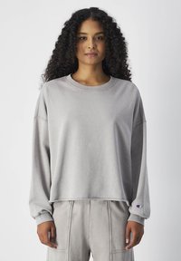 Grijze cropped sweatshirt met lange mouwen, gemaakt van zacht materiaal, met een ronde halslijn en geribbelde manchetten. Champion logo op de mouw.