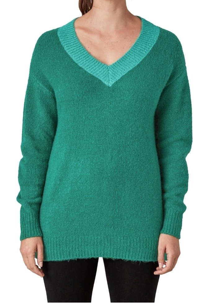 Femme portant un pull en maille duveteuse col en V bleu sarcelle avec manches longues et poignets côtelés, associé à un pantalon noir.