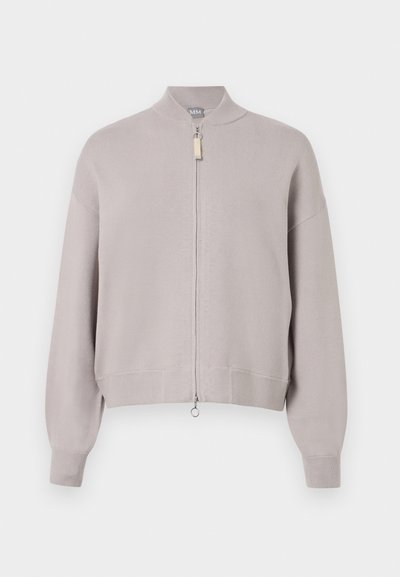 Šviesiai pilkas užtrauktuko kardiganas, pagamintas iš minkštos mezginio medžiagos. Yra aukšta apykaklė ir raukšlėtos rankogaliai, sidabrinis užtrauktukas ir mažas traukimo antgalis.